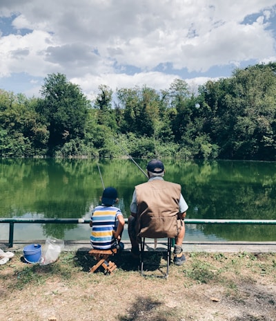 man in black shirt sitting on chair near lake during daytime