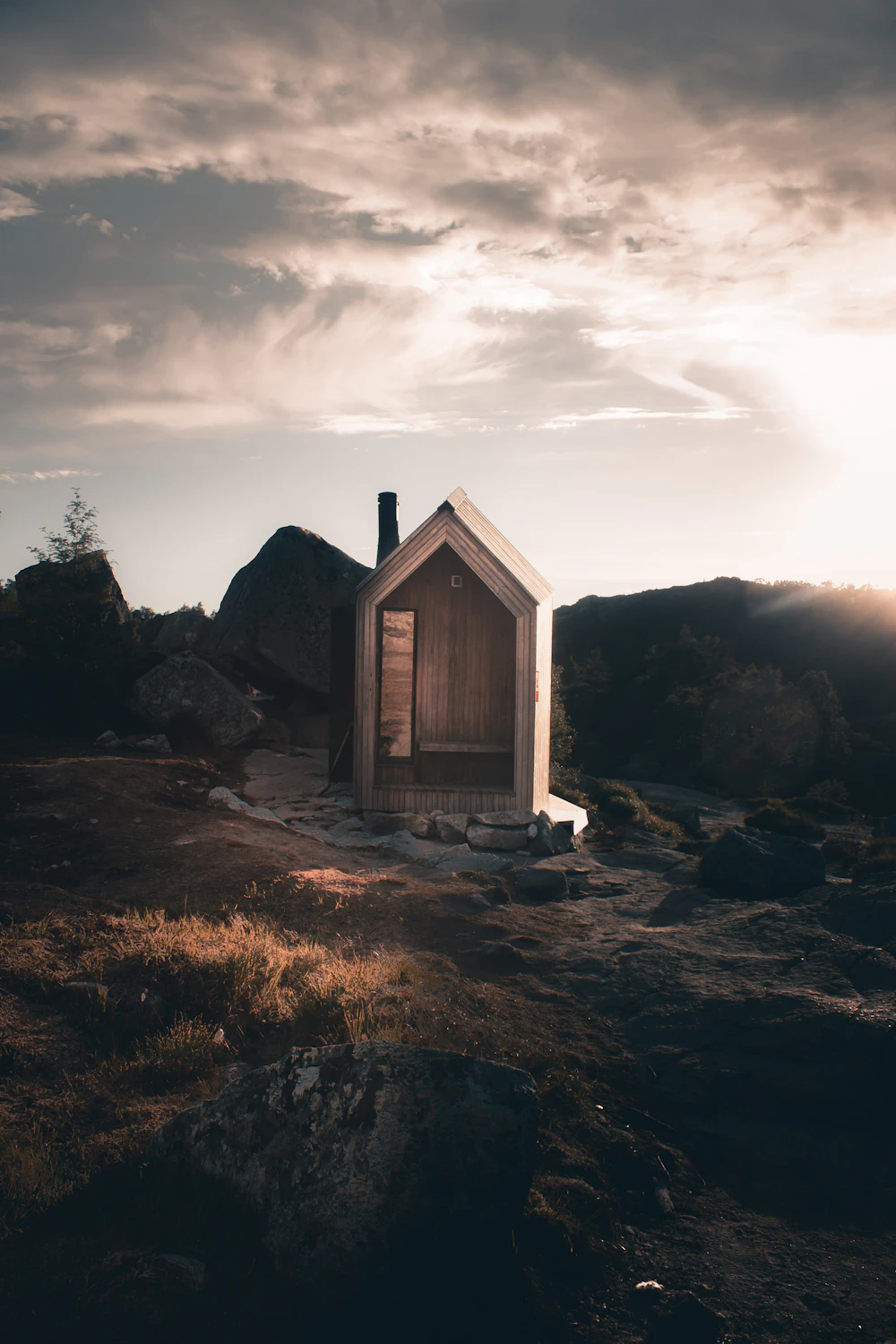 Mørkt trehus på svaberg under skyet himmel