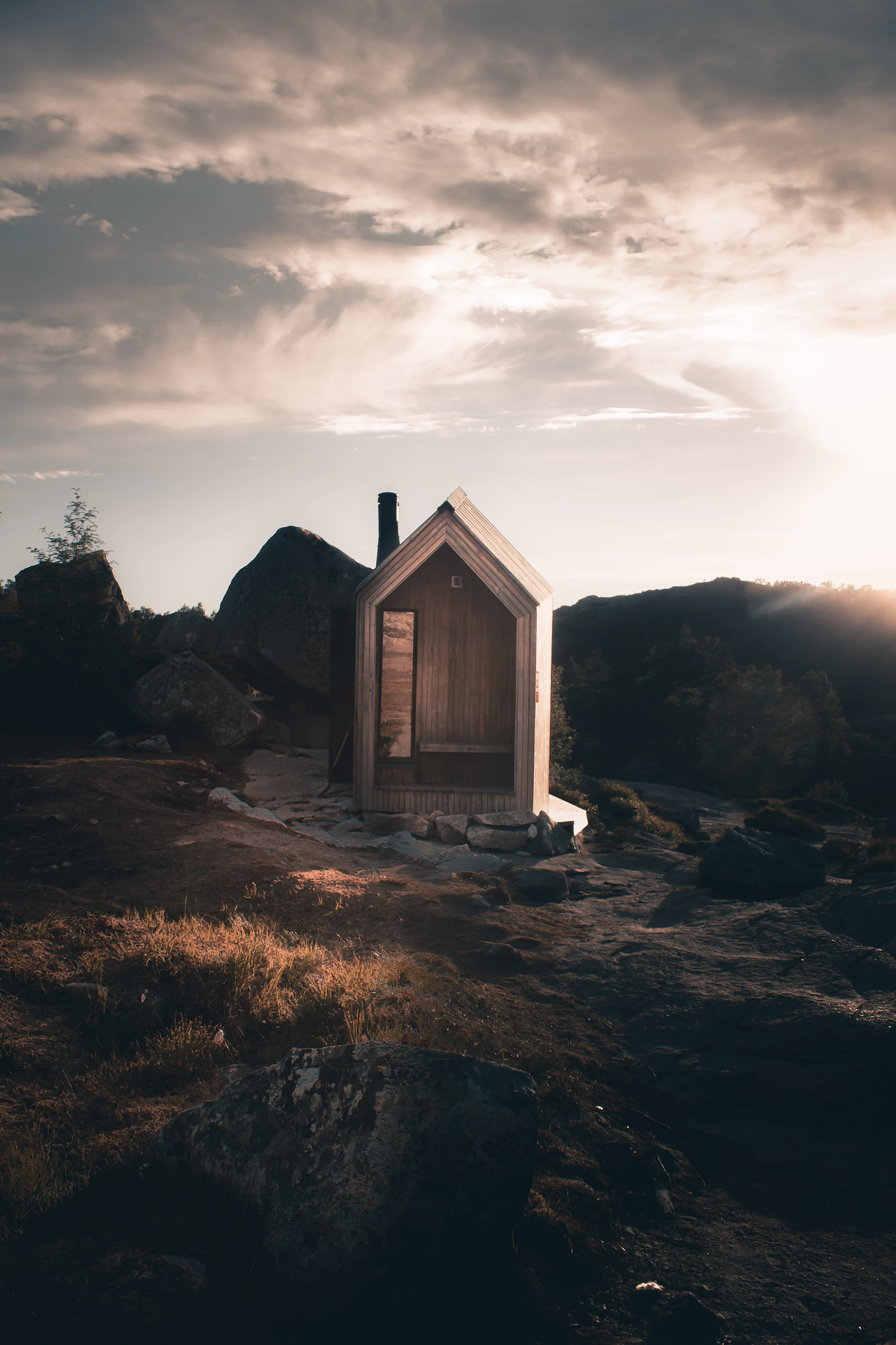 Mørkt trehus på svaberg under skyet himmel