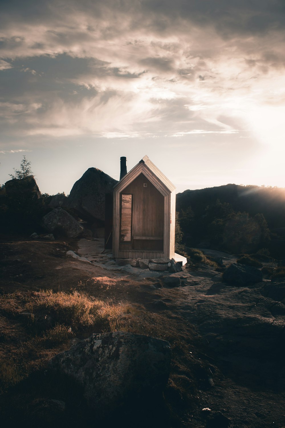 brown wooden house on rocky ground under gray cloudy sky