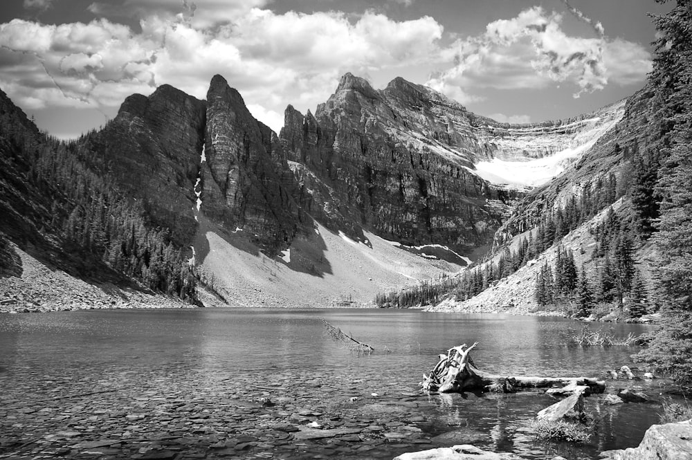 grayscale photo of person riding on boat on lake near rocky mountain