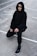 A person wearing a black hooded sweatshirt and pants crouches on a concrete surface, with distinctive black eye makeup resembling a mask. The setting appears to be an outdoor basketball court, evident from the white boundary lines. The facial expression is serious, adding an enigmatic vibe.