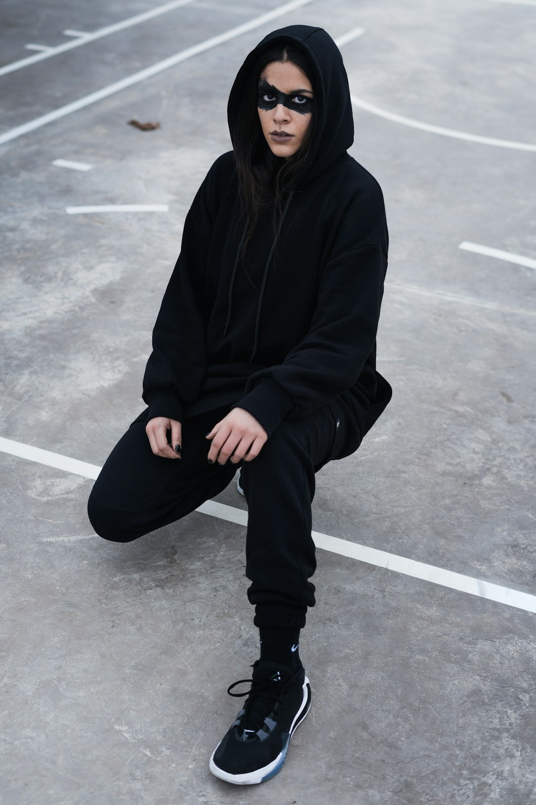 woman in black hoodie and black pants sitting on gray concrete floor