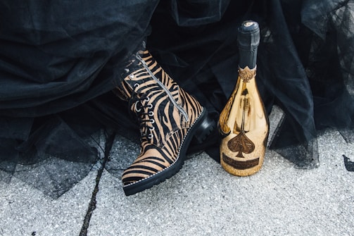 Close-up of a pair of deep maroon, gold-detailed boots resting on a marble pedestal.