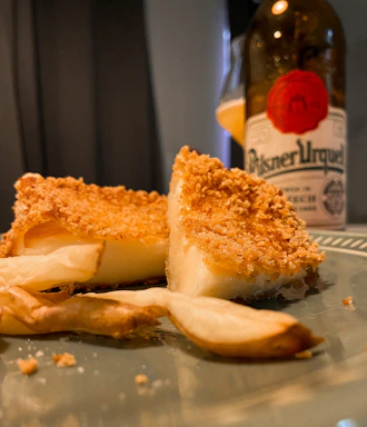 Close-up photo of a rustic wooden board with pickled hermelin cheese, utopenci sausages, and a glass of craft beer in a cozy industrial pub setting.