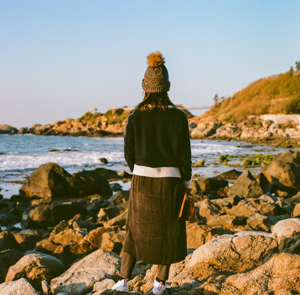 woman in black jacket standing on rocky shore during daytime