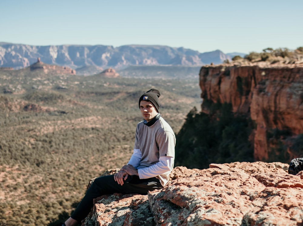 man in white dress shirt and black pants sitting on brown rock during daytime