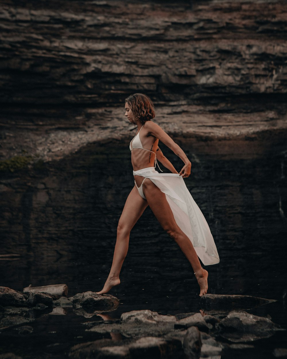 woman in white dress walking on rocky shore during daytime