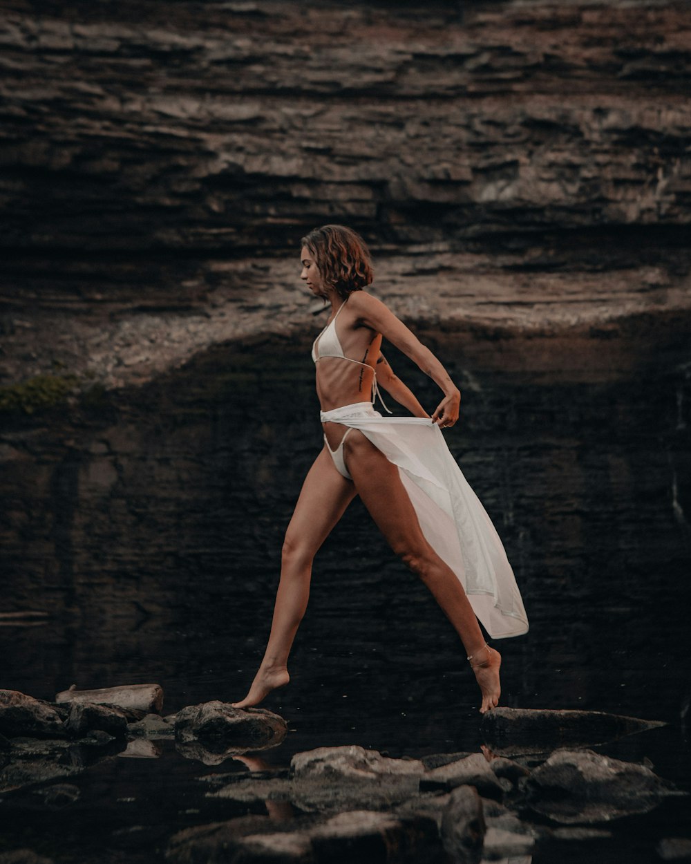 Mujer en vestido blanco caminando en la orilla rocosa durante el día