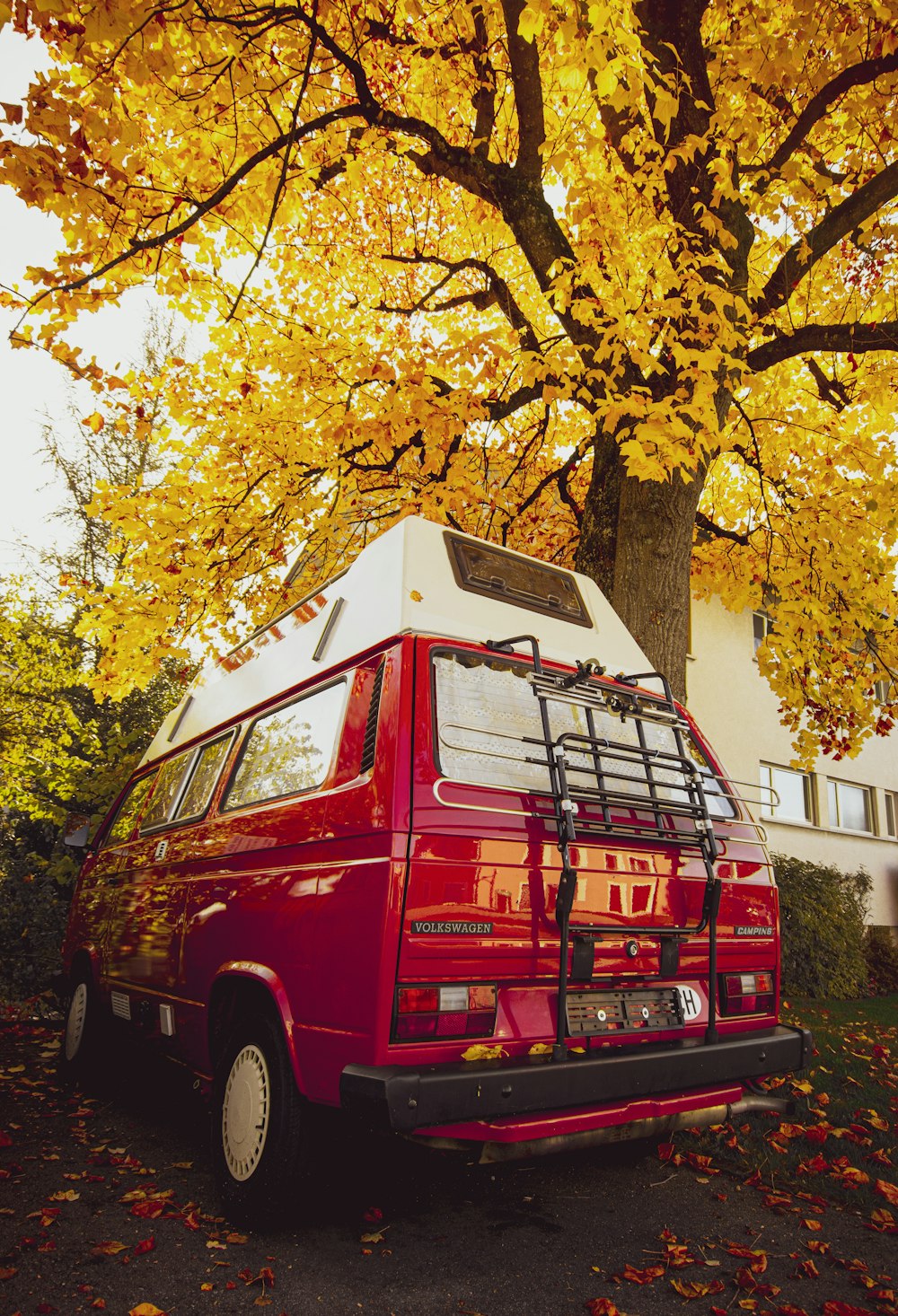 furgone rosso parcheggiato accanto all'albero a foglia gialla