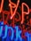 Brightly glowing neon lights in red and blue with a reflective surface creating a vibrant and colorful display. The neon tubes are formed in various shapes and letters, giving an abstract appearance.