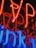 Brightly glowing neon lights in red and blue with a reflective surface creating a vibrant and colorful display. The neon tubes are formed in various shapes and letters, giving an abstract appearance.