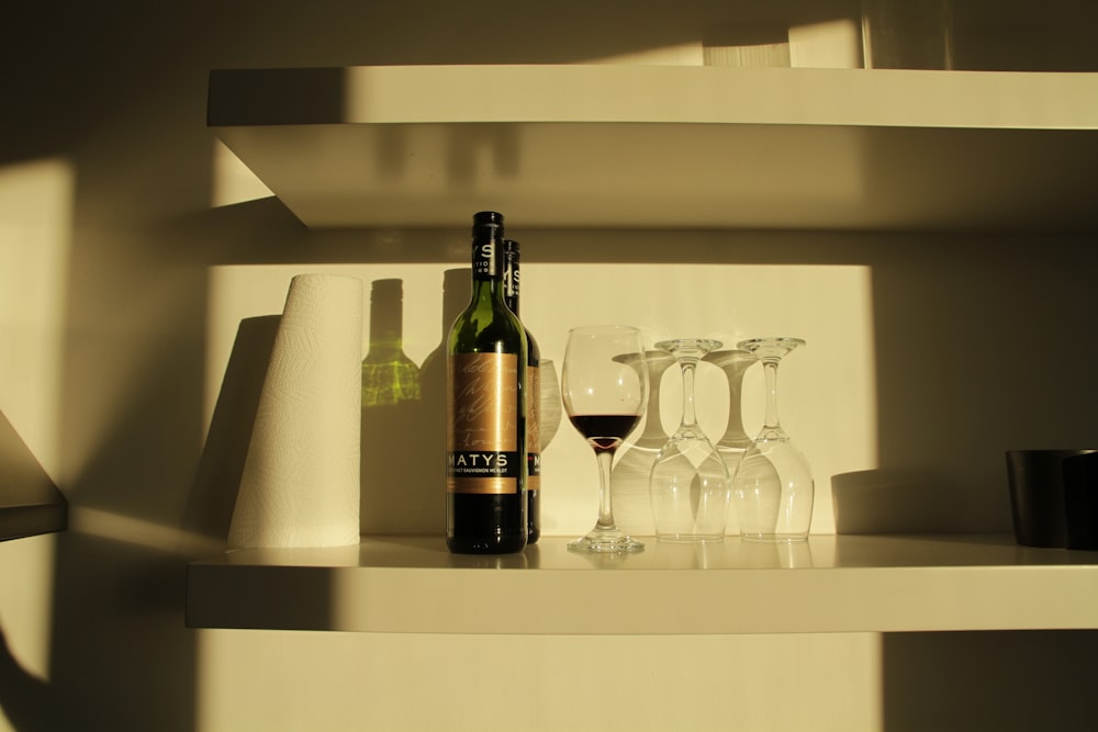 wine bottle beside wine glass on white wooden shelf