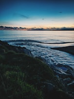 Soft waves lapping against a rocky shore at dusk, the horizon melting into a palette of muted blues and grays.