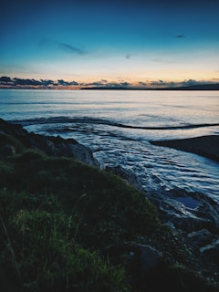 Soft waves lapping against a rocky shore at dusk, the horizon melting into a palette of muted blues and grays.