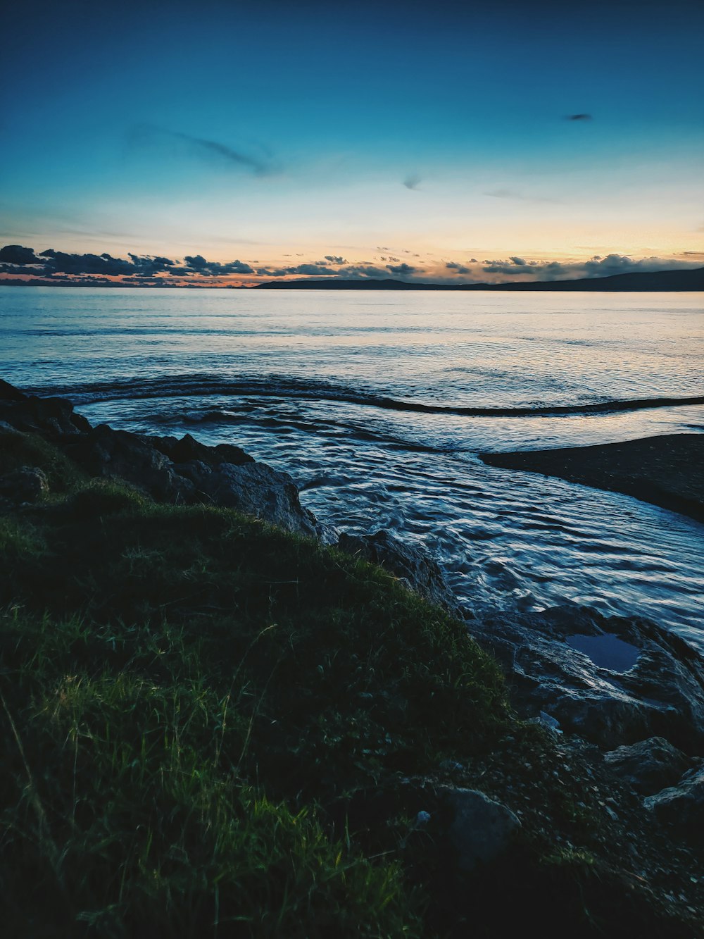 green grass near body of water during sunset