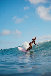 A woman surfing on a pink board on a blue ocean wave