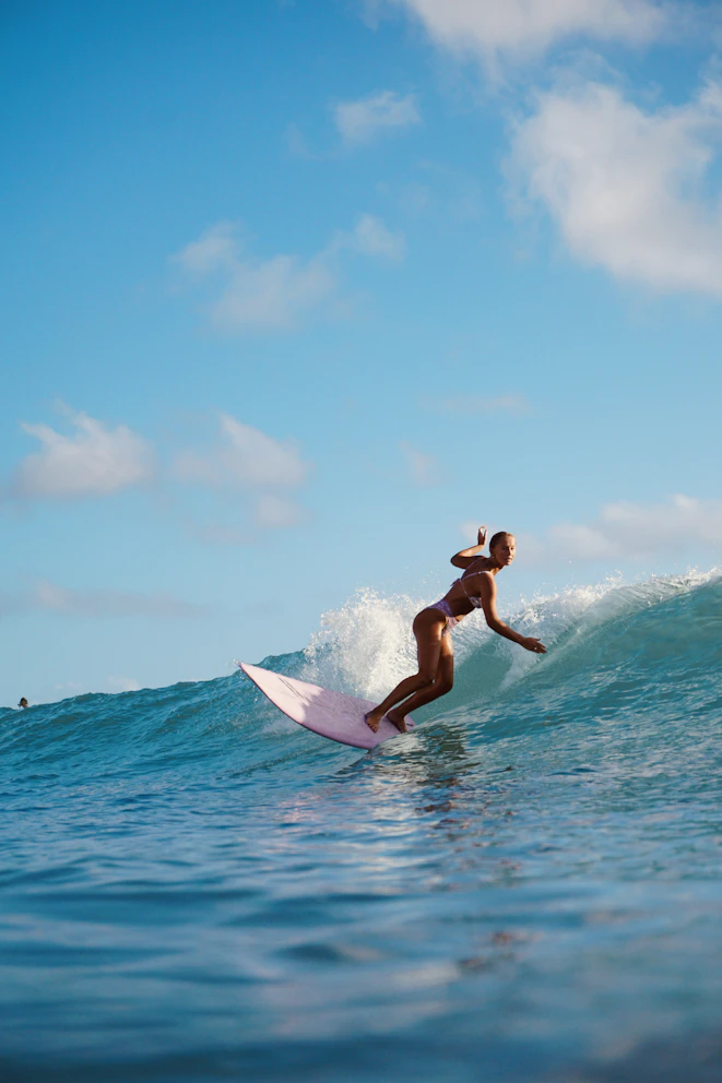 A woman surfing on a pink board on a blue ocean wave