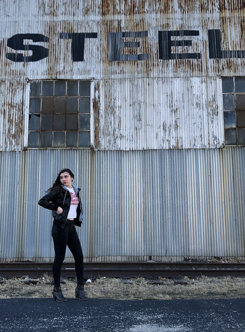 woman in black jacket and black pants standing beside white wooden wall during daytime