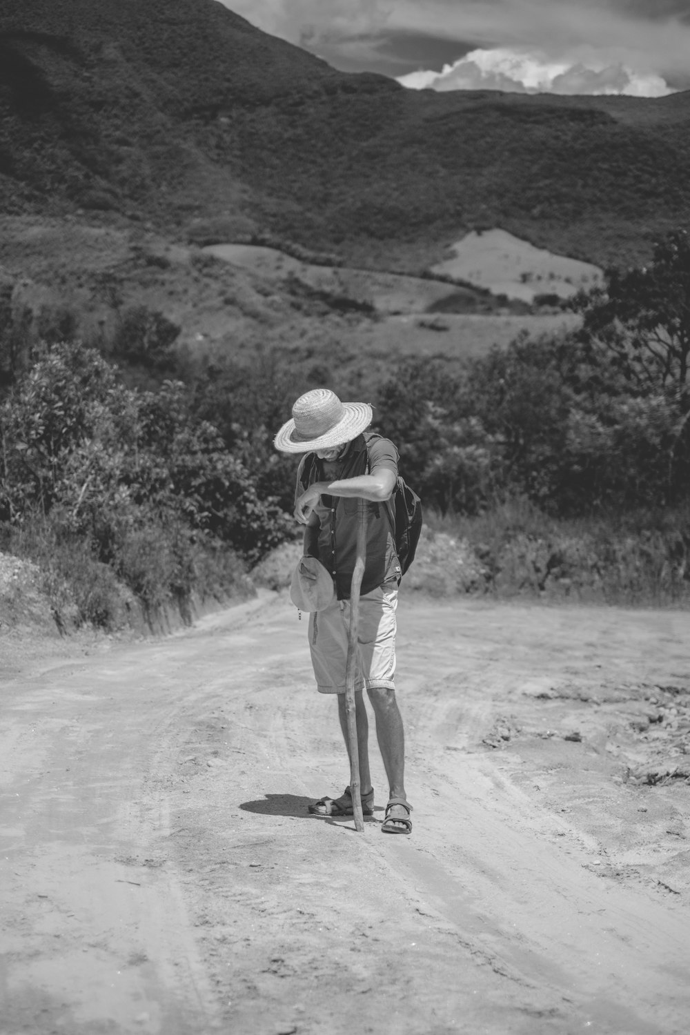 man in black shirt and brown pants wearing white hat walking on dirt road during daytime