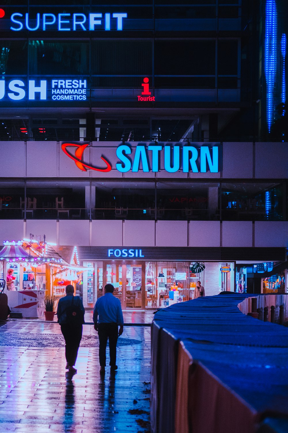 a couple of people walking down a wet sidewalk