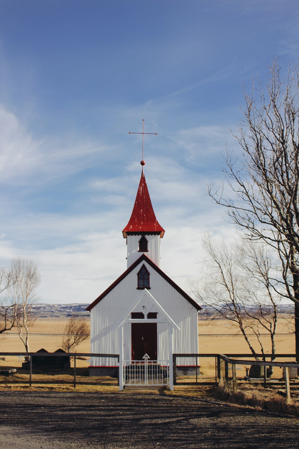 white and red church near bare trees under blue sky during daytime