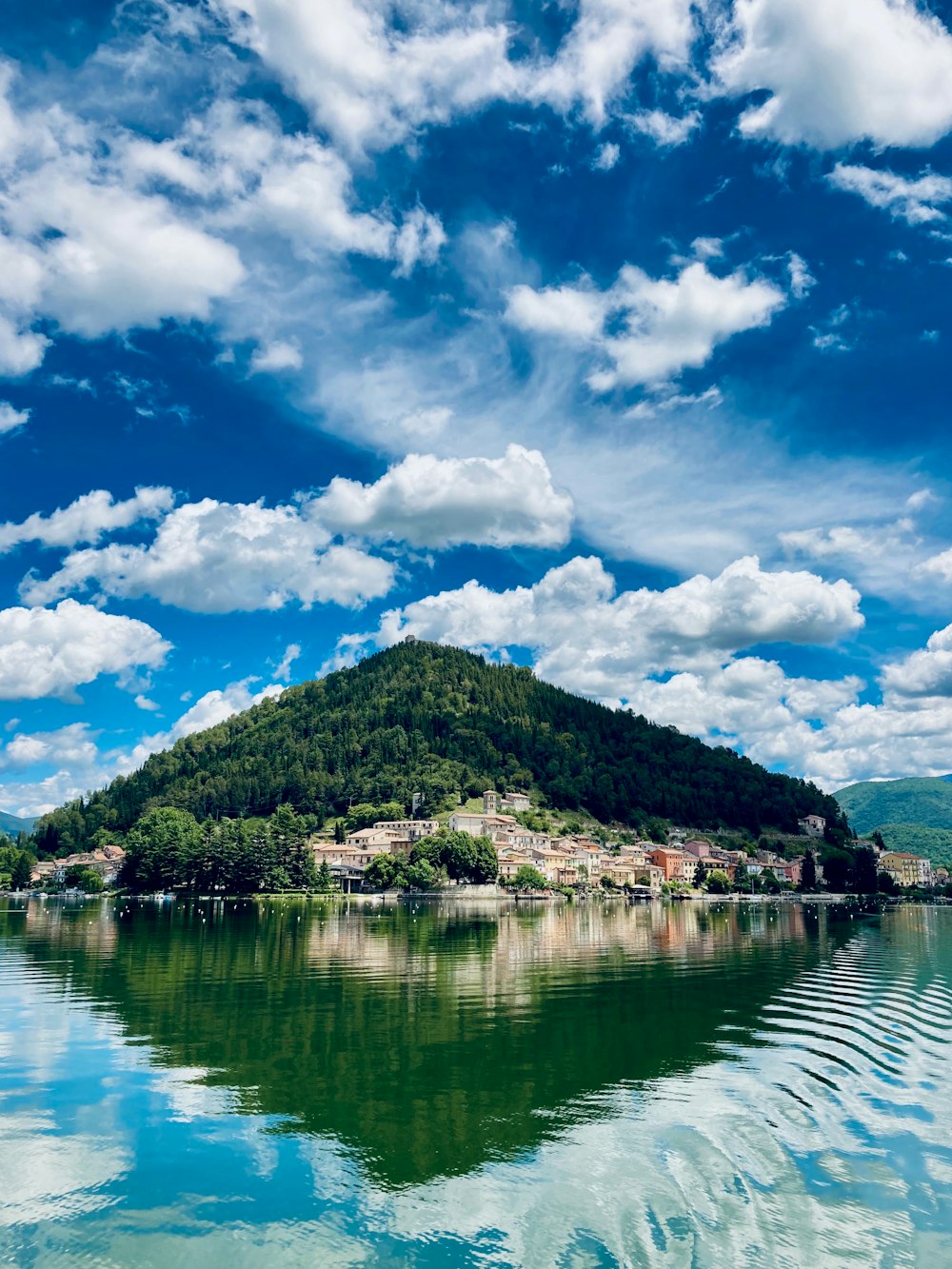 green and brown mountain beside body of water under blue and white cloudy sky during daytime