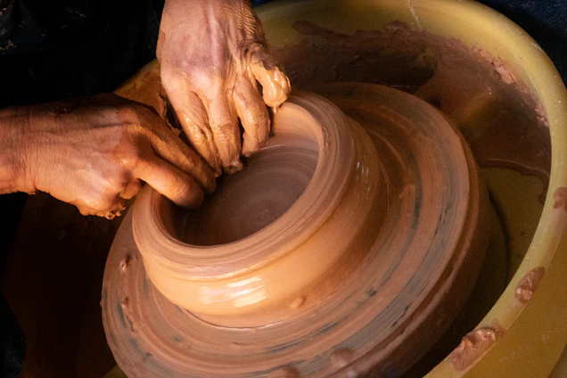 A warm studio scene showing hands shaping a bright, glossy ceramic bowl on a spinning wheel.