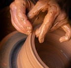 Artisan shaping natural clay on a potter’s wheel, hands covered in soft beige clay