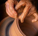Hands gently shaping clay on a potter’s wheel, surrounded by soft sunlight.
