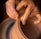Hands covered in clay delicately shape a pot on a potter’s wheel, showcasing the intricate craft of pottery making. The brown, wet clay spins smoothly as the fingers mold it with precision.