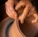 Hands covered in clay delicately shape a pot on a potter’s wheel, showcasing the intricate craft of pottery making. The brown, wet clay spins smoothly as the fingers mold it with precision.