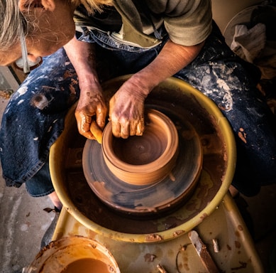 person in blue denim jeans making clay pot