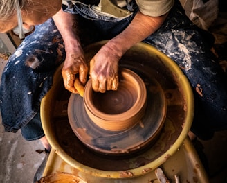 person in blue denim jeans making clay pot
