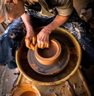 person in blue denim jeans making clay pot