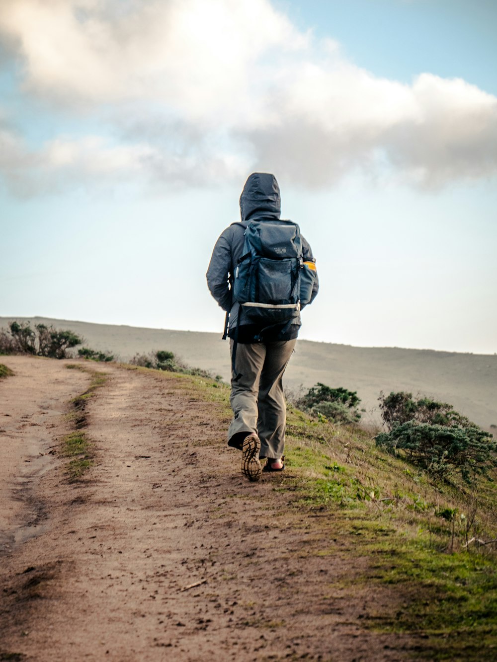 person in gray hoodie walking on brown dirt road during daytime