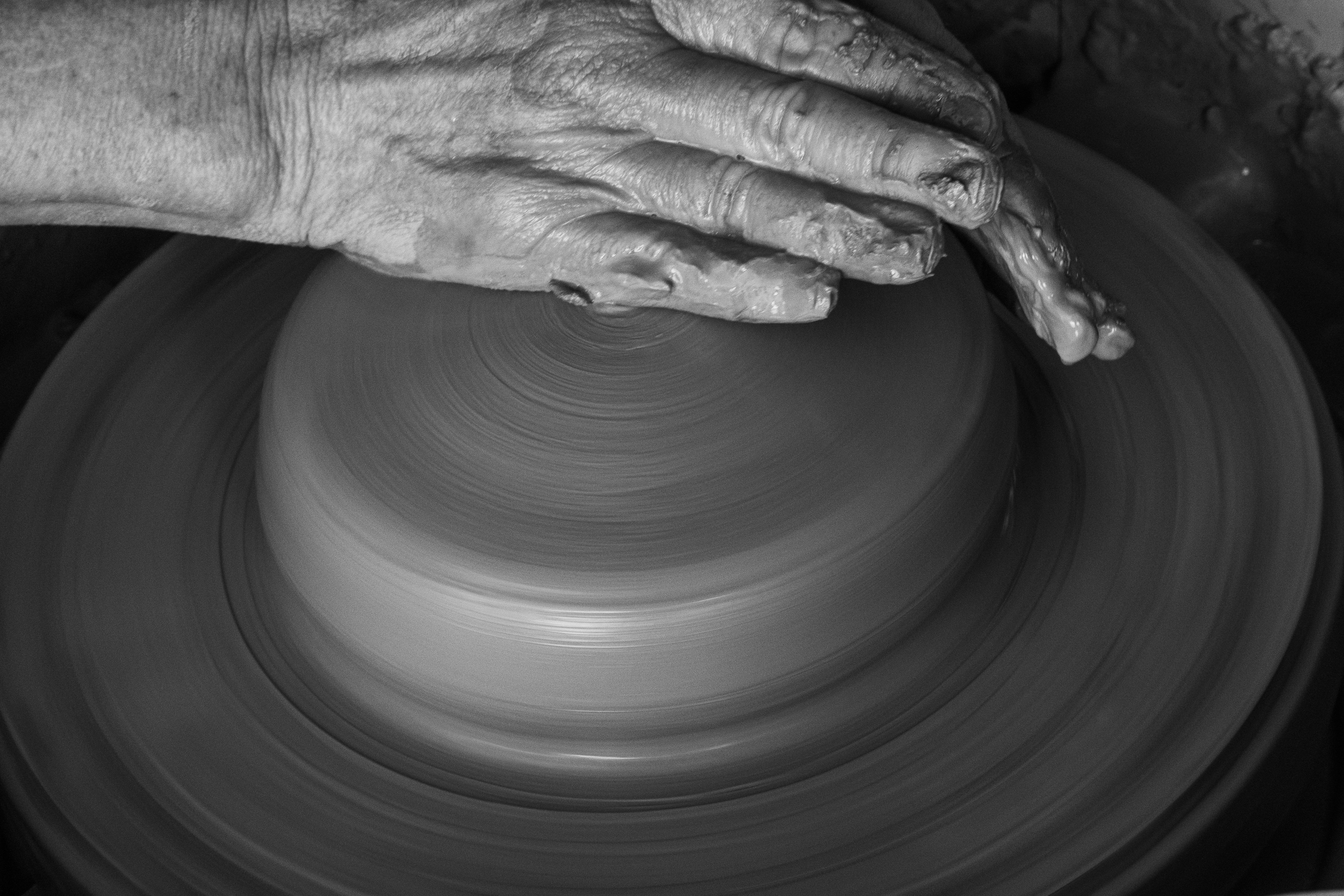 Hands shaping a lump of clay on a potter’s wheel, with soft natural light highlighting the texture.