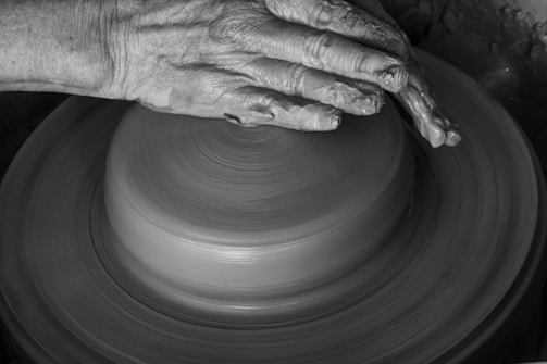 Hands of a person shaping clay on a pottery wheel, highlighting the artistic crafting process. The image captures the detailed texture of the clay and the focus and skill involved in pottery-making.