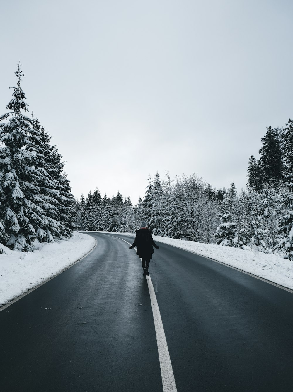 person in black jacket walking on snow covered road during daytime