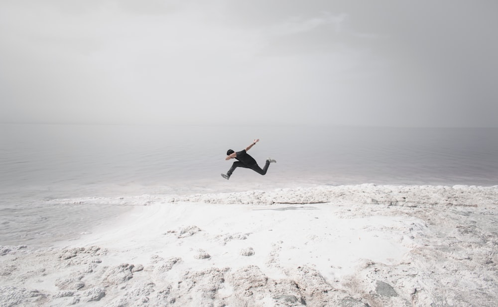 man in black shirt and black pants jumping on white sand beach during daytime