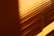 Warm shadows of window blinds create a striped pattern on a wall, with sunlight casting a gradient from dark to light.