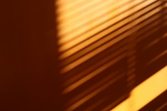 Warm shadows of window blinds create a striped pattern on a wall, with sunlight casting a gradient from dark to light.