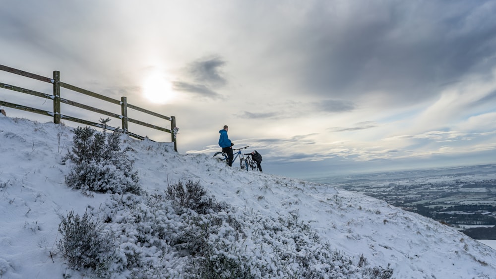 person in blue jacket and black pants sitting on black wooden fence on snow covered ground