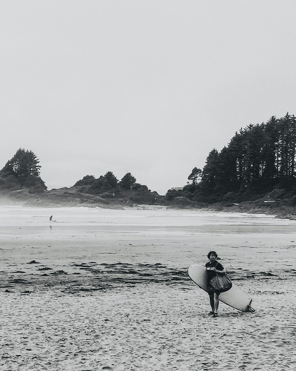 Persona con camisa negra que lleva una tabla de surf blanca caminando por la playa durante el día