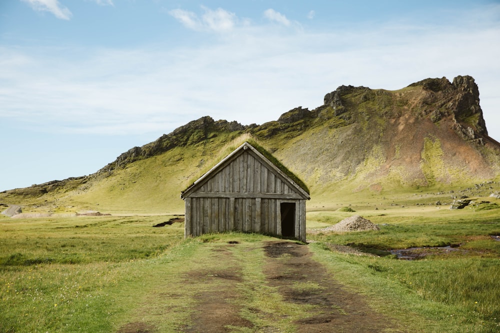 brown wooden house on green grass field near mountain under white clouds during daytime