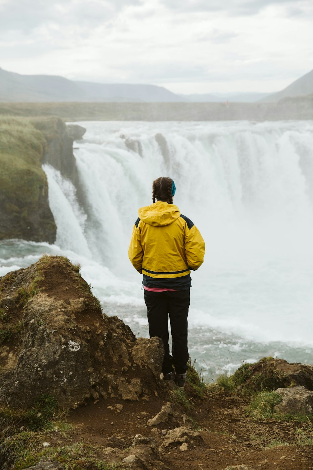 man in yellow hoodie standing in front of waterfalls