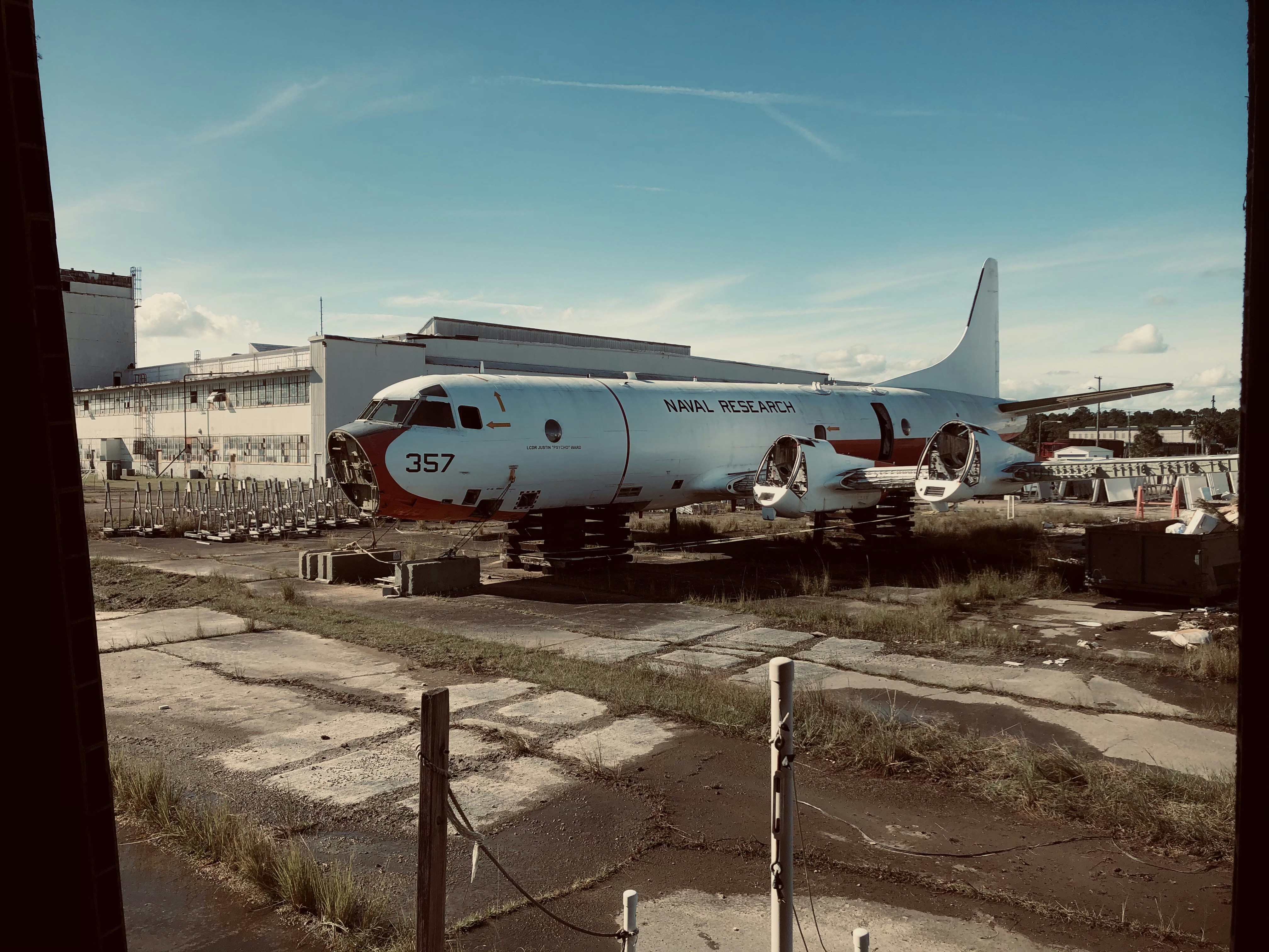 white passenger plane on brown field during daytime, the shell of a p3 Orion sub hunter aircraft, This former patrol aircraft would make long sorties to hunt for hidden submarines. what was once a hunter-killer of the seas is now a ghost of its past. now left abandoned under the sky.