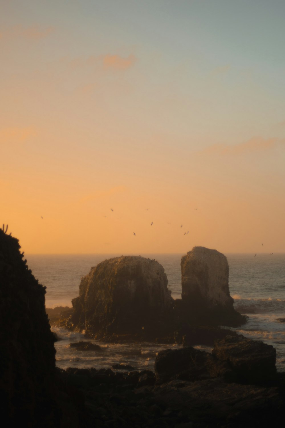 silhouette of rock formation on sea during sunset