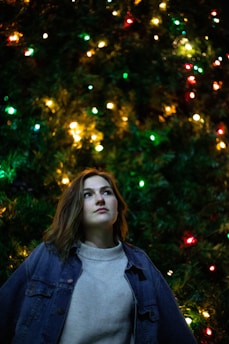 woman in gray turtleneck shirt standing beside green christmas tree
