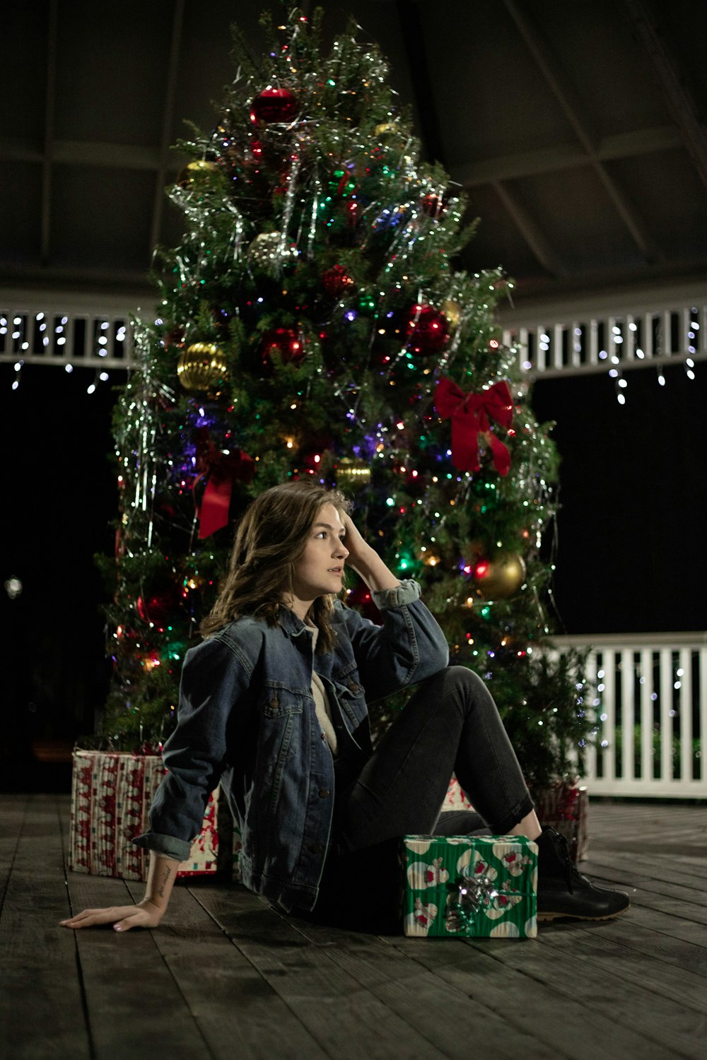 woman in black jacket sitting on chair beside christmas tree